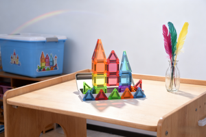 Colorful geometric building blocks on a wooden table with a rainbow in the background