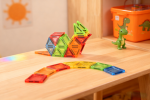 Colorful magnetic building blocks on a wooden surface with a dinosaur toy in the background.